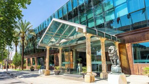 A modern building with a glass facade, palm trees, and a covered entrance with columns. - Checkin Camino de Granada (Granada)