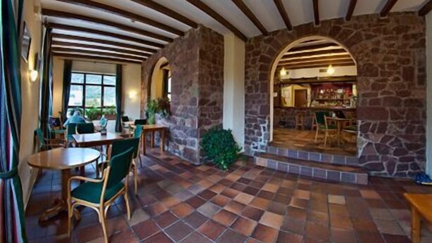 Un restaurante acogedor con paredes de piedra, vigas de madera y suelo de baldosas. Hay mesas y sillas para comer.