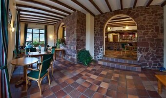 Un restaurante acogedor con paredes de piedra, vigas de madera y suelo de baldosas. Hay mesas y sillas para comer.