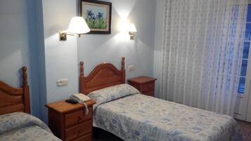 A hotel room with two wooden beds, a nightstand with a telephone, and a wall-mounted lamp.