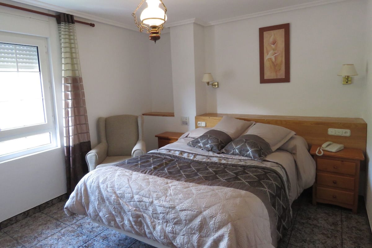 Une chambre d’hôtel avec un lit, une chaise, une table de chevet, une lampe et un tableau au mur.