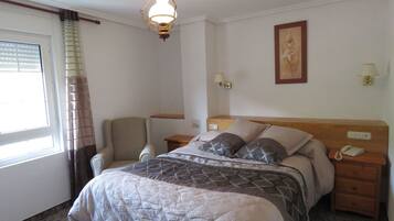 A hotel room with a bed, a chair, a nightstand, a lamp, and a painting on the wall.