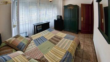 A bedroom with a bed, a television on a stand, a wardrobe, and a door.