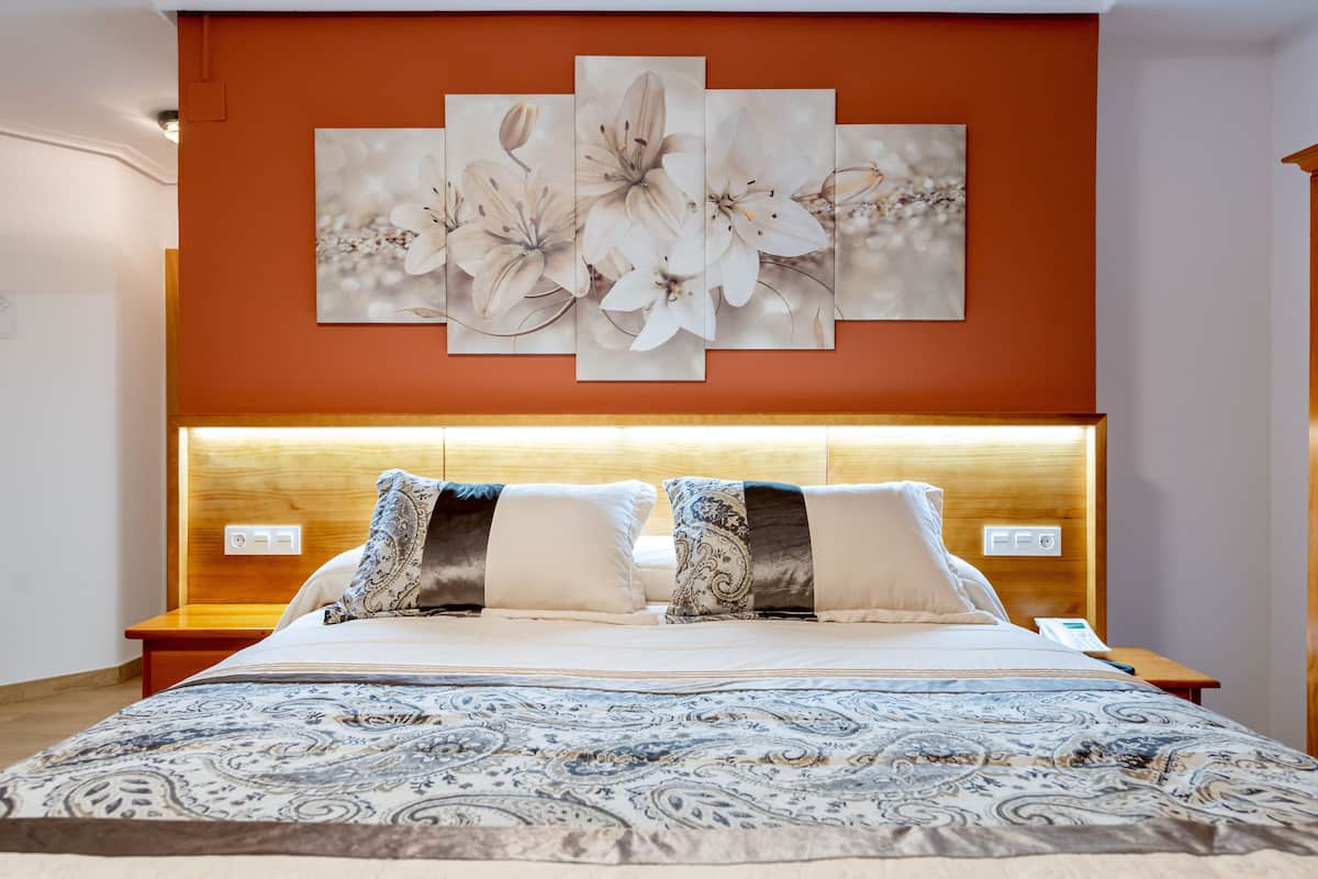 Un lit bien fait, recouvert d’une couvre-lit à motifs, avec une tête de lit en bois et une œuvre d’art florale accrochée au mur au-dessus.