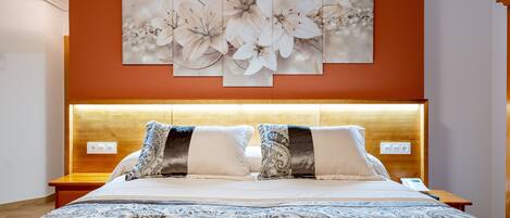 A neatly made bed with a patterned bedspread, a wooden headboard, and a wall-mounted floral artwork above it.