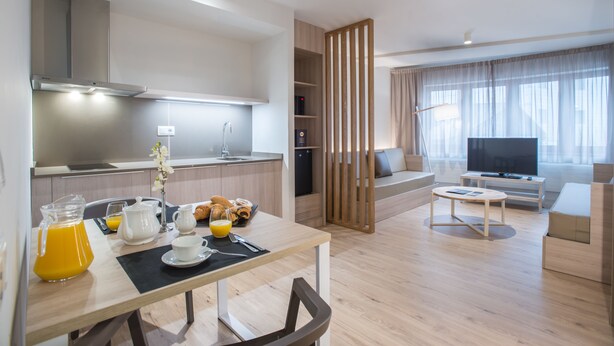Una sala de estar moderna con televisor, sofá y mesa de centro. Se observa una cocina con estufa y pileta.