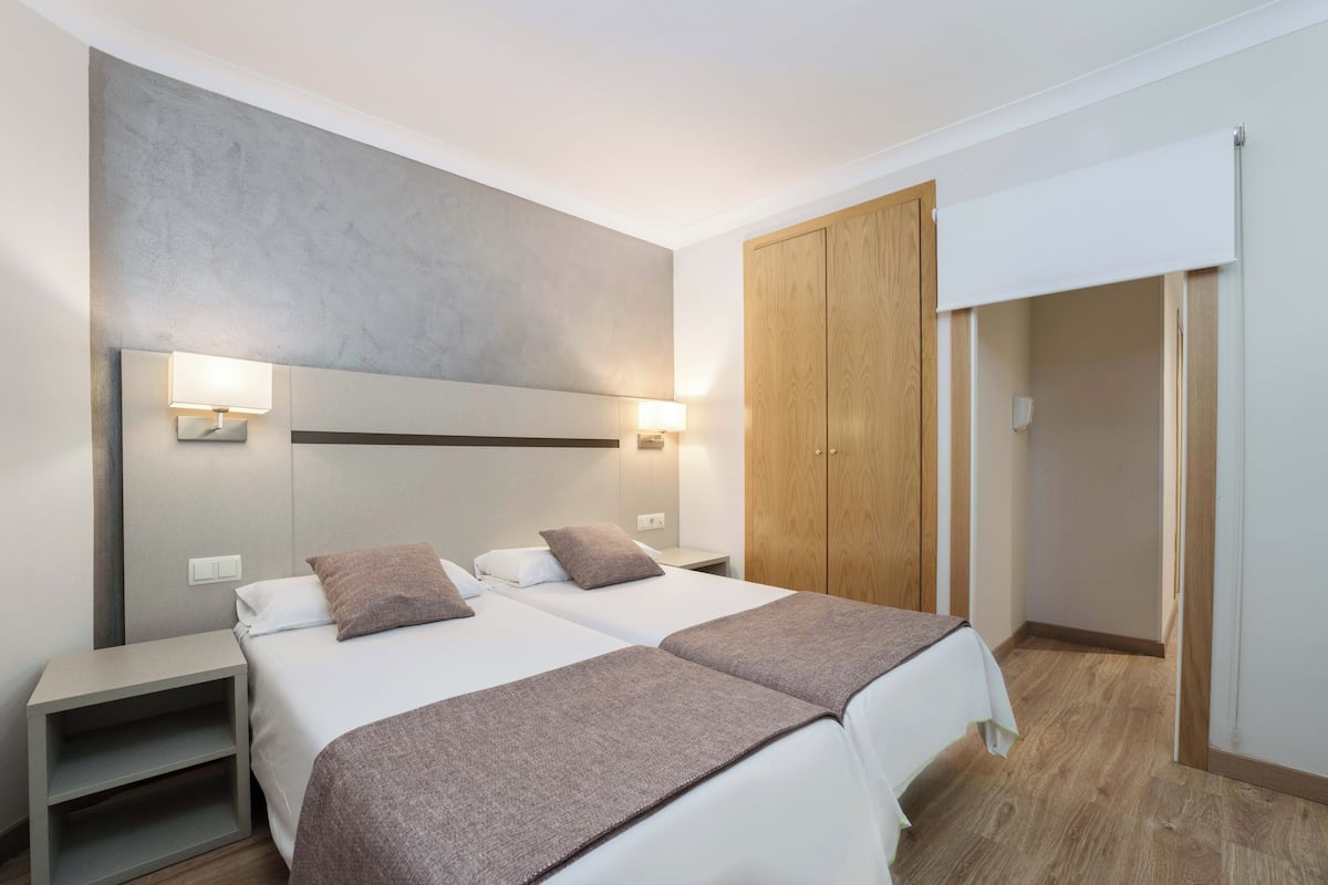 A modern hotel room with two beds, a wooden wardrobe, and a sliding door.