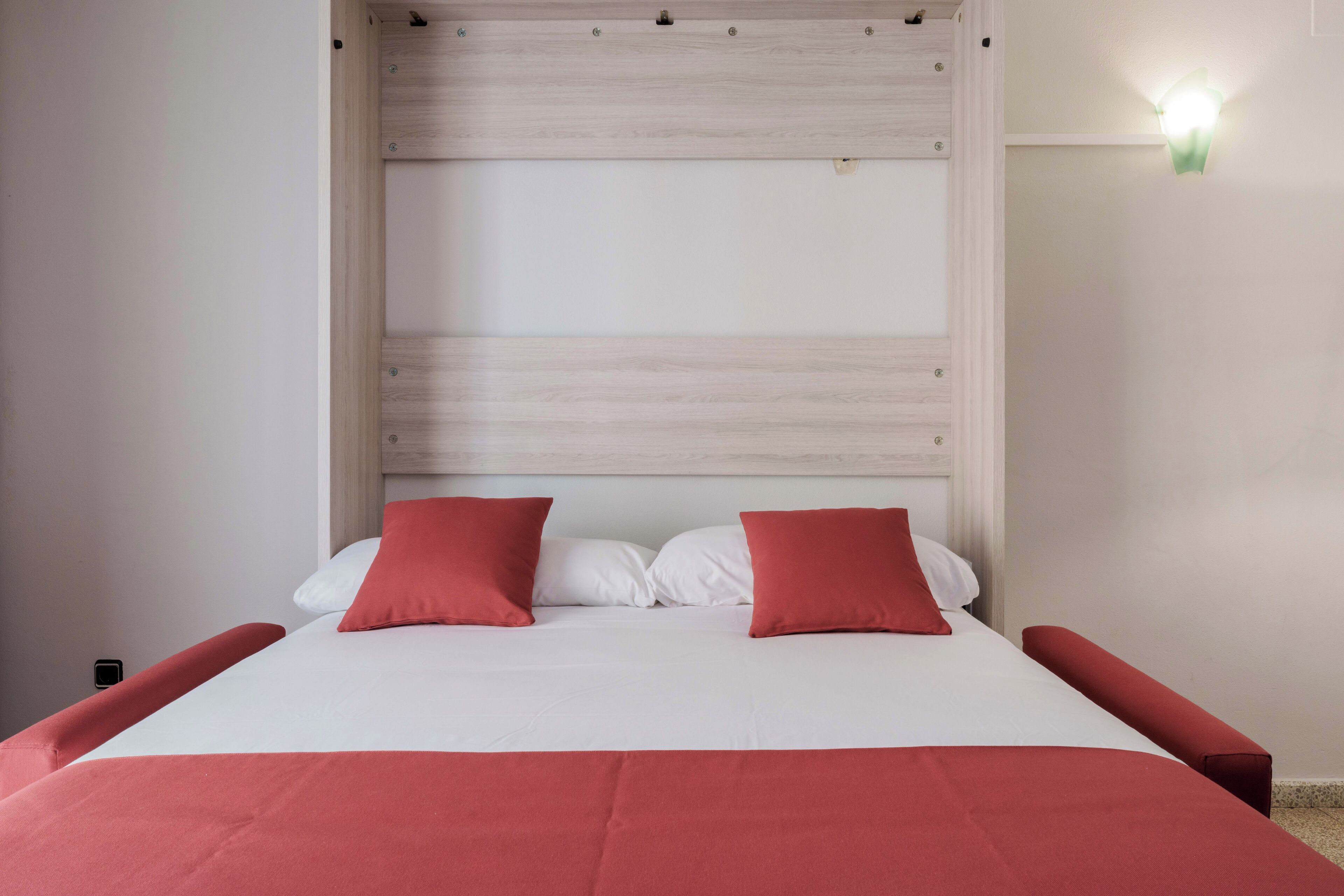 Ein Bett mit einem Holz-Kopfteil, zwei roten Kissen und einer weißen Bettdecke.