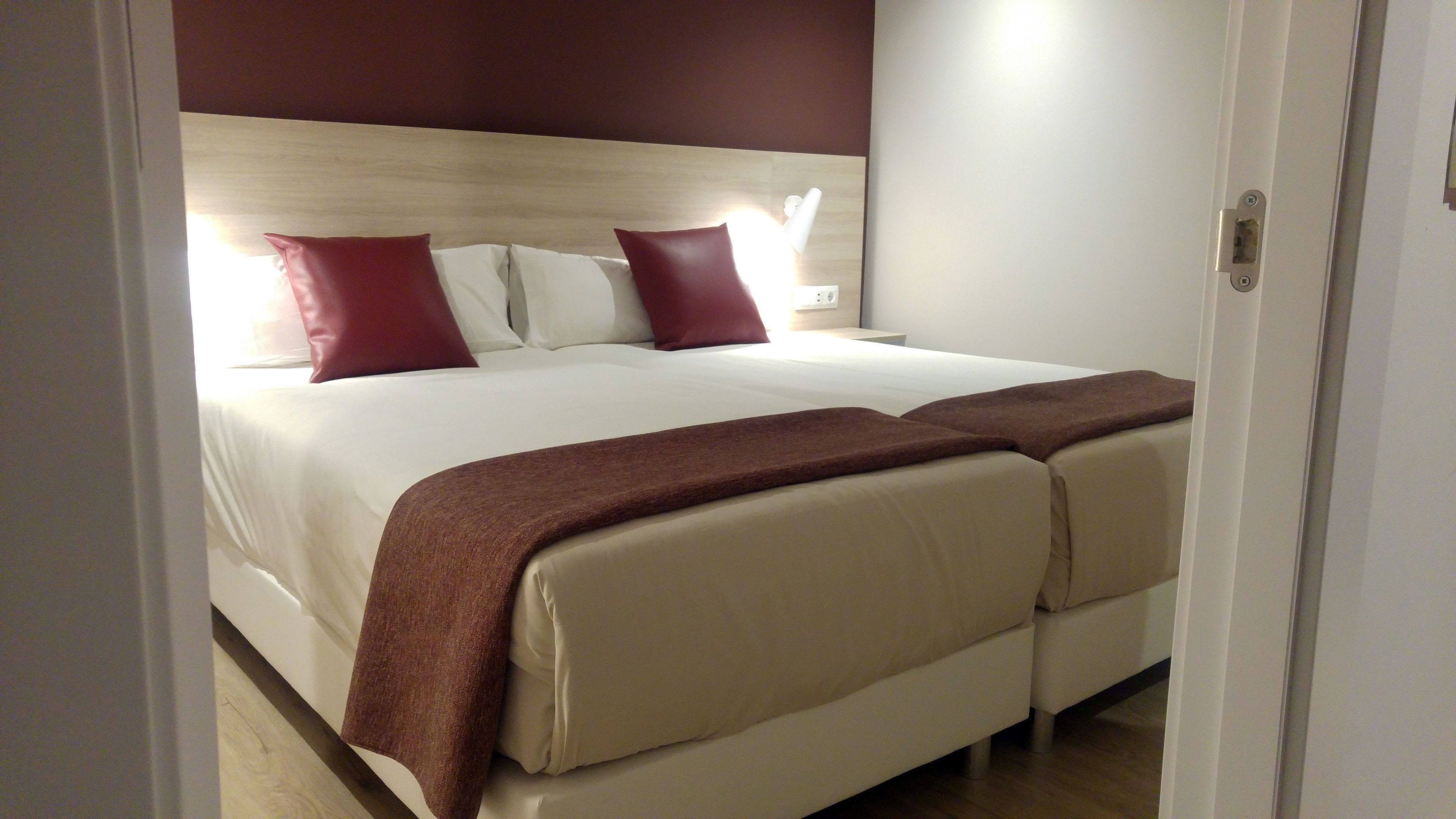 Cama doble con cabecera de madera, dos almohadas rojas y una manta marrón.