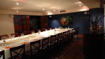 A long dining table set for a meal with chairs, a vase with flowers, and a painting on the wall.