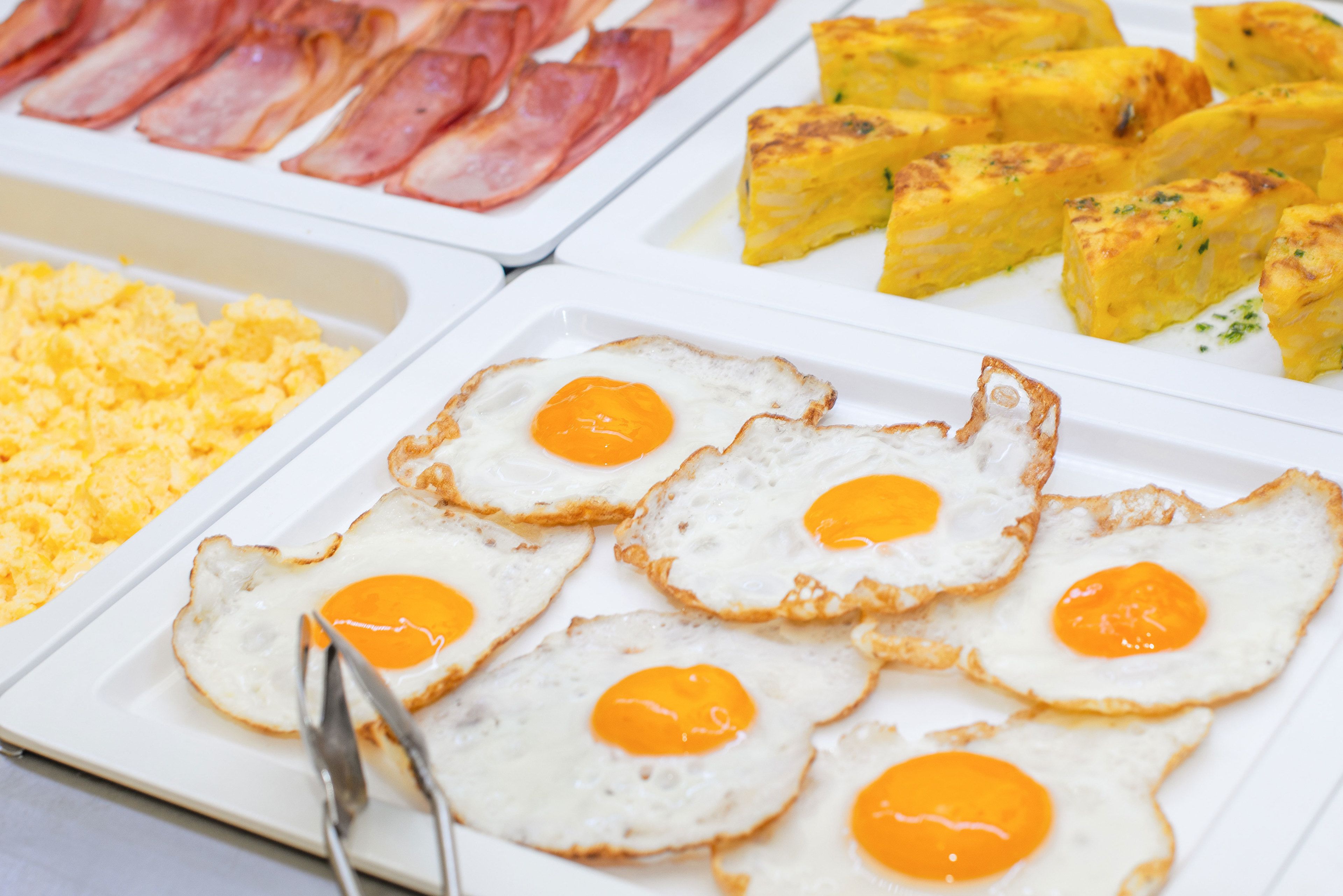 A breakfast buffet with scrambled eggs, bacon, and omelettes.