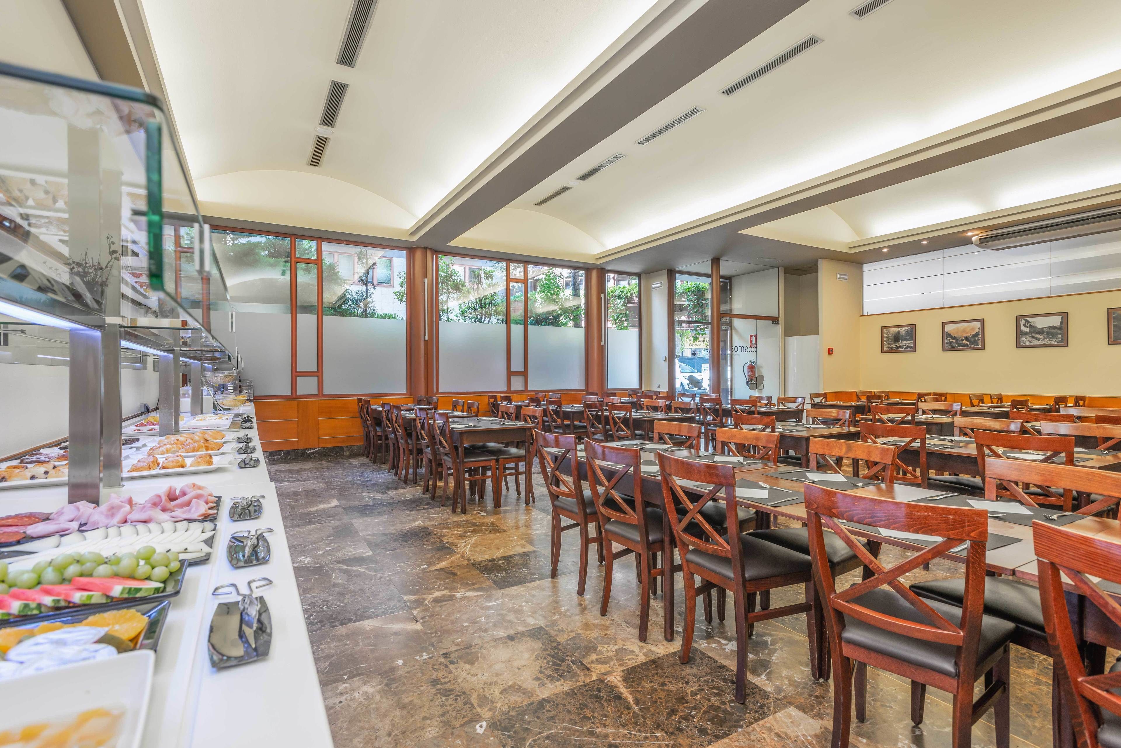 A buffet-style restaurant with multiple dining tables and chairs, a variety of food items on display, and large windows allowing natural light.