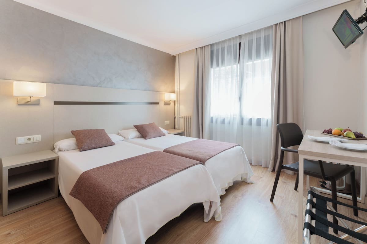 A hotel room with two beds, a desk, a chair, and a television.