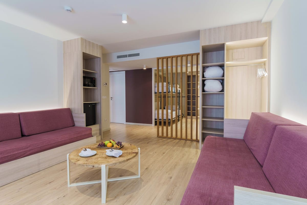 A modern living room with a wooden floor, a round coffee table with fruits, a purple sofa, and a wooden wardrobe with shelves.