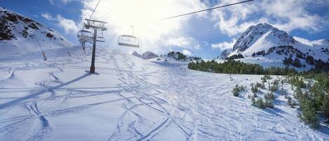A ski slope with a ski lift, snow-covered mountains, and tracks in the snow.