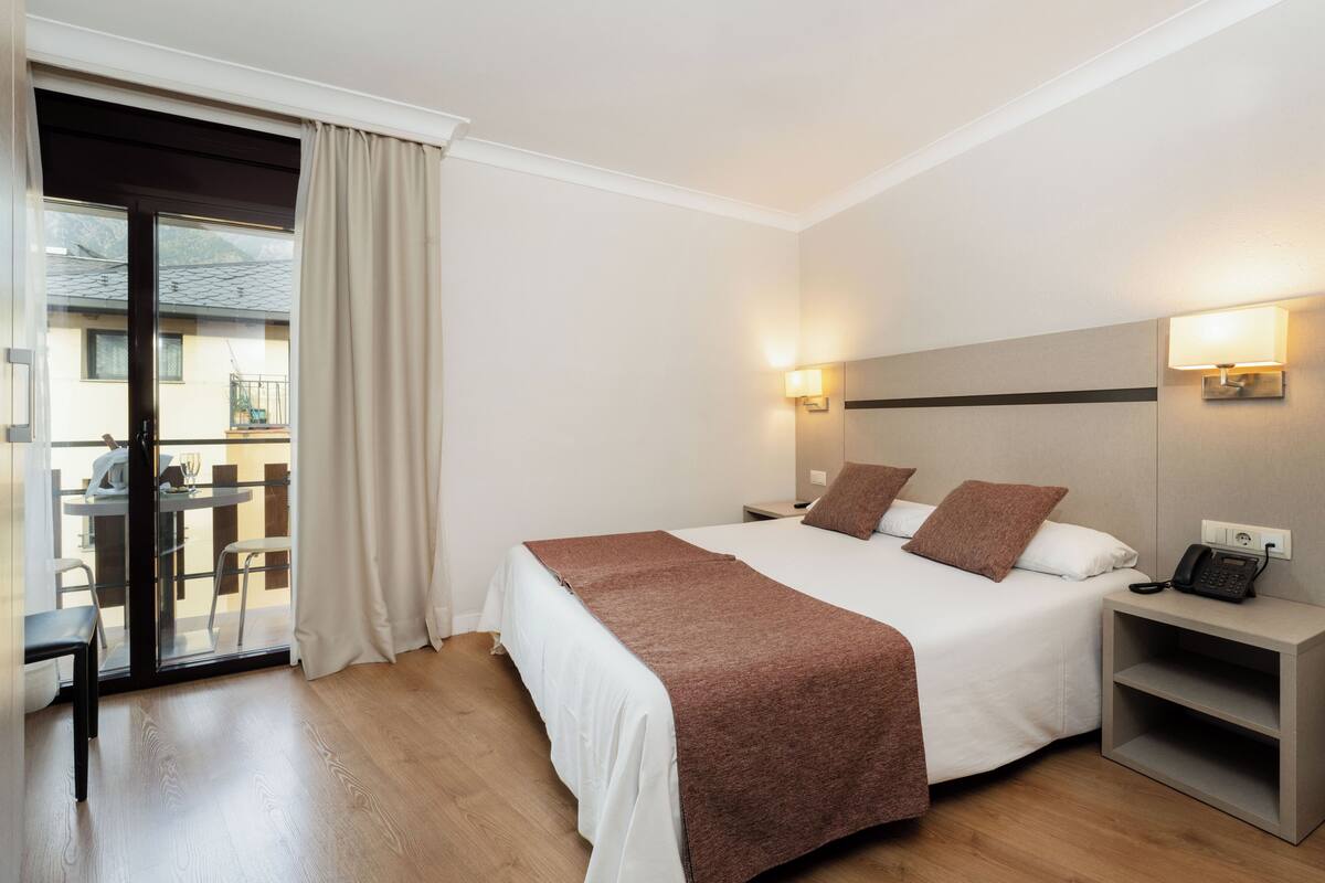 A hotel room with a bed, bedside tables, a desk, and a view of the outside balcony.
