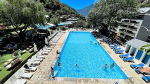 Una piscina con sillas de descanso y sombrillas, rodeada de edificios y árboles.