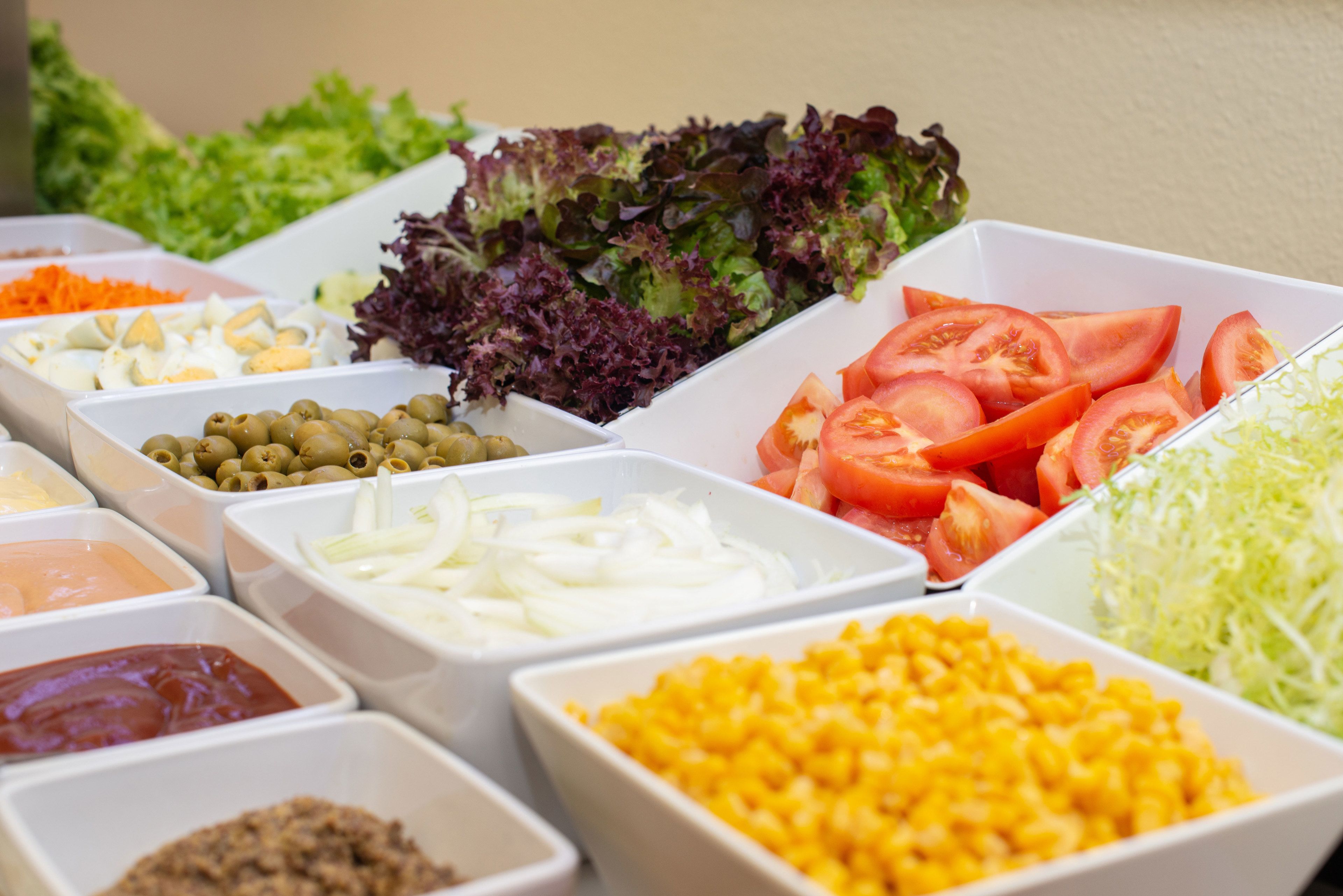Variedad de alimentos en recipientes blancos, incluyendo verduras, queso y salsas.