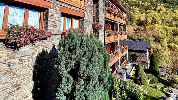 A multi-story building with stone walls and wooden balconies adorned with flowers. - Hotel & SPA Bringué (El Serrat)