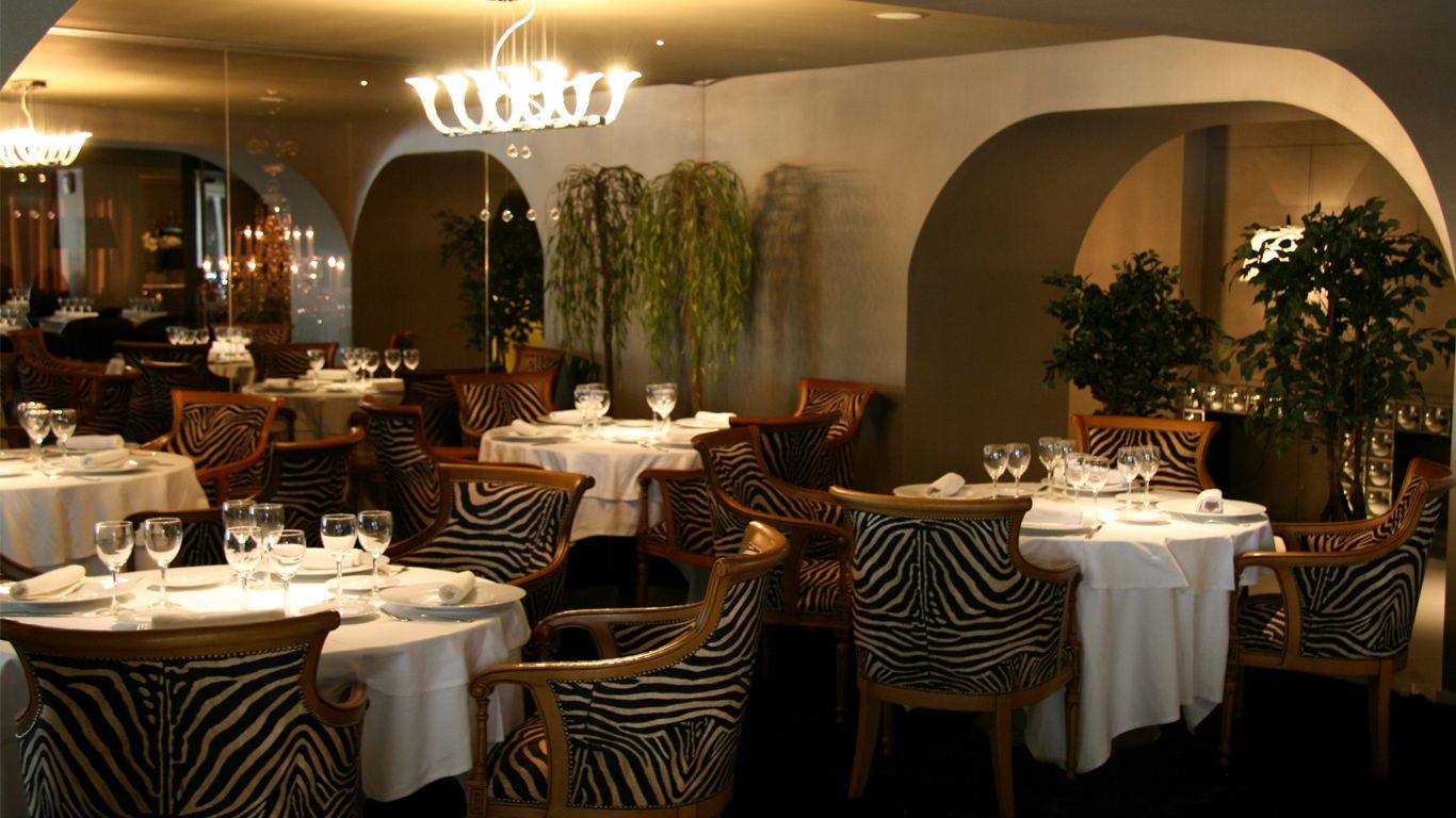 Un restaurante con sillas a rayas de cebra, manteles blancos y una araña.