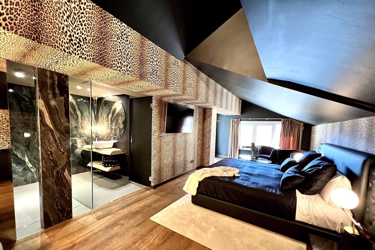 A modern bedroom with a large bed, a glass-enclosed bathroom, and a view of the outdoors.