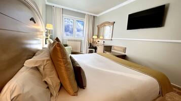 A hotel room with a large bed, a desk, a chair, a TV mounted on the wall, and a window with curtains.