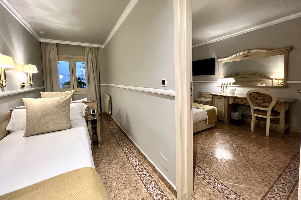 A hotel room with a bed, bedside table, lamp, and a desk with a chair.