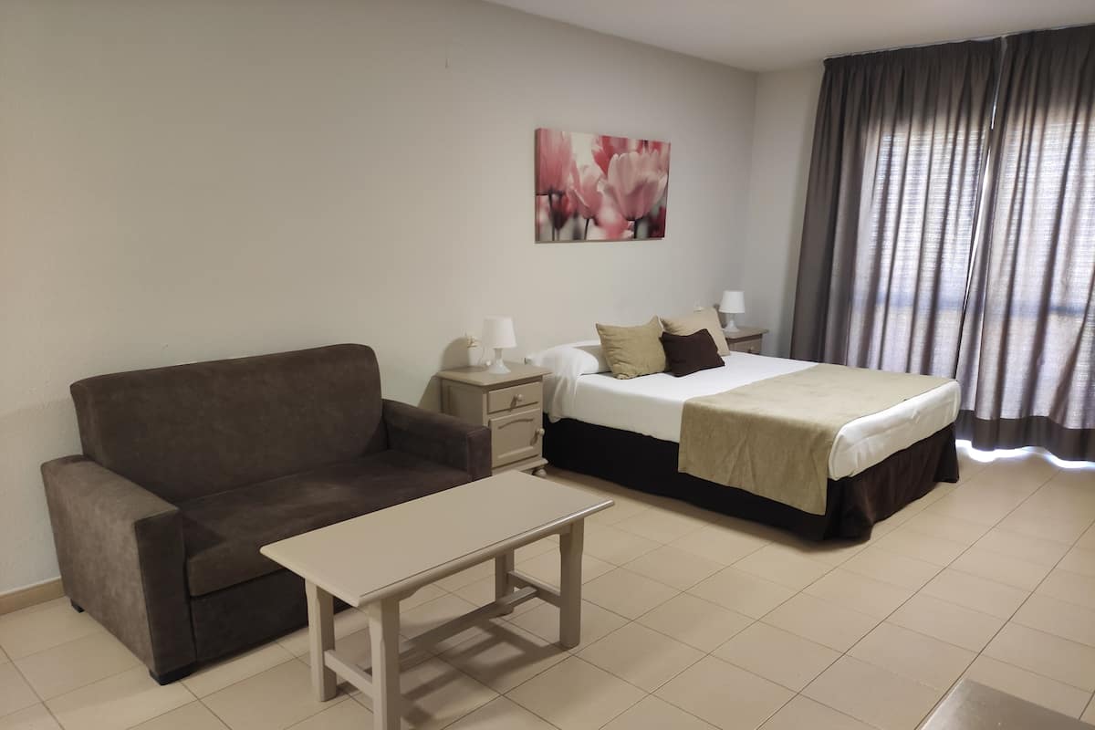 A hotel room with a bed, a sofa, a nightstand, a lamp, and a painting on the wall.