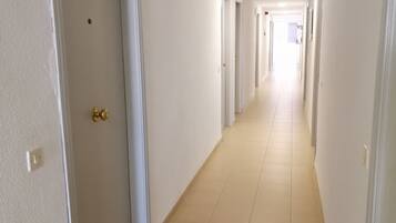 A long, narrow hallway with white walls and tiled floors, leading to multiple doors.
