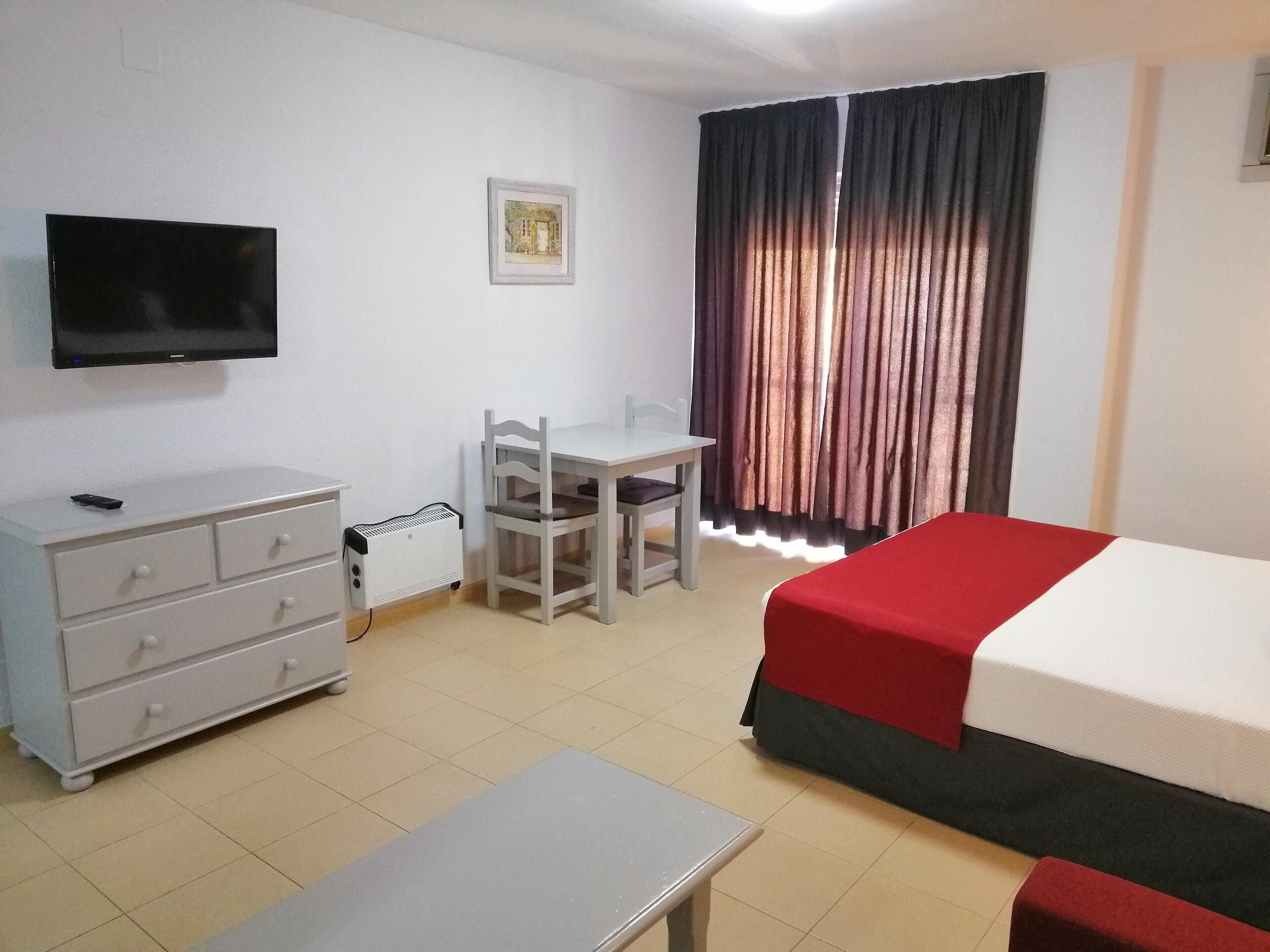 Una habitación de hotel con cama, escritorio, silla, televisor y cómoda.