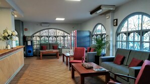 Un hall d’entrée avec un comptoir de réception, un espace détente comprenant des canapés et des fauteuils, une table basse et de grandes fenêtres agrémentées d’éléments décoratifs en fer forgé.