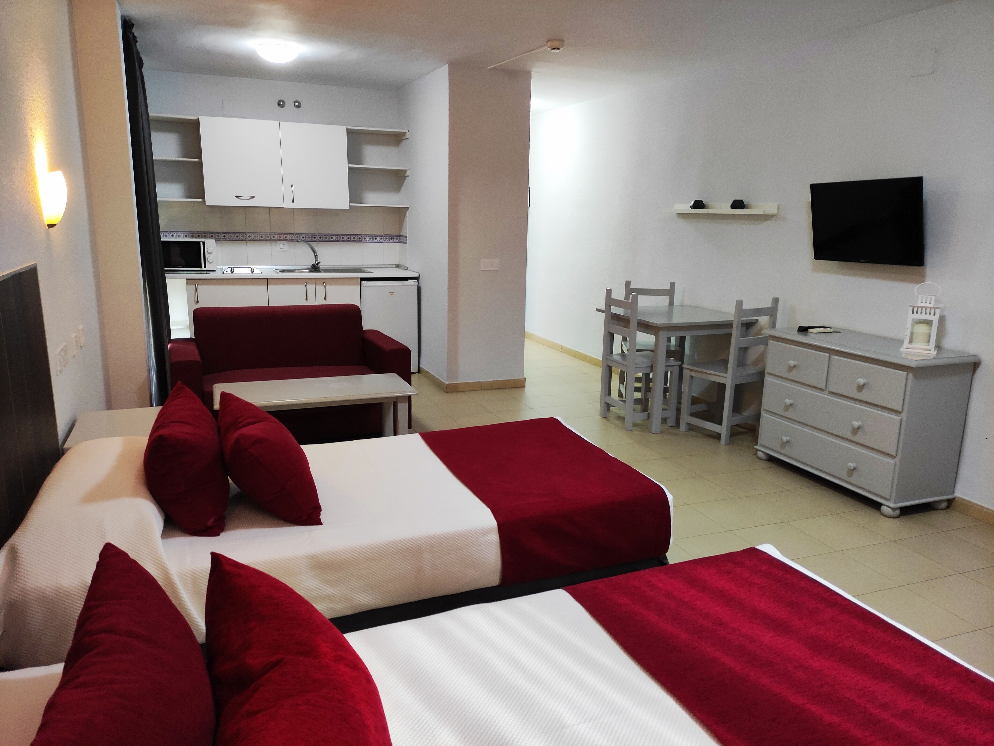 Una habitación de hotel con dos camas, una kitchenette pequeña, una mesa de comedor con sillas, un televisor y un aparador.