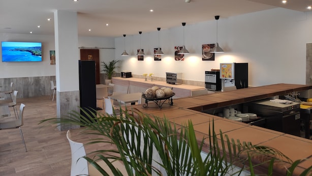Un hall d’hôtel moderne avec un long comptoir d’accueil, un espace salon et un grand téléviseur à écran plat diffusant des images d’un paysage pittoresque.