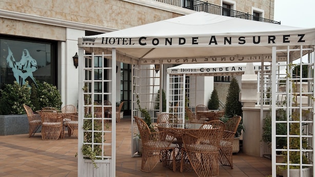 Un área de estar al aire libre con techo, mobiliario de mimbre y un letrero que dice "HOTEL CONDE ANSUREZ".
