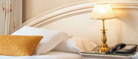 A neatly made bed with white linens, a single gold-colored lamp, and a telephone on a bedside table.