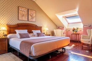 Un dormitorio con una cama grande, dos lámparas de noche, una mesita de noche de madera, una silla, una pequeña mesa con un jarrón y un tragaluz.