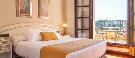 A hotel room with a bed, a nightstand, a lamp, and a balcony with chairs.