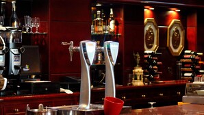 Una zona de bar con dos grifos de cerveza, una máquina de café y una estantería con vino al fondo.