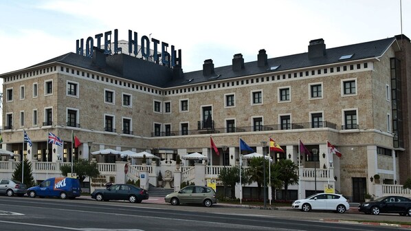 Un hotel con un letrero llamativo, varias banderas y un estacionamiento con varios coches.