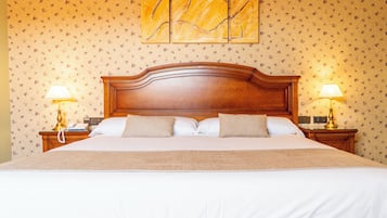 Een net opgemaakt bed met een houten hoofdbord, twee bedlampen en een behang met een bloemendesign.