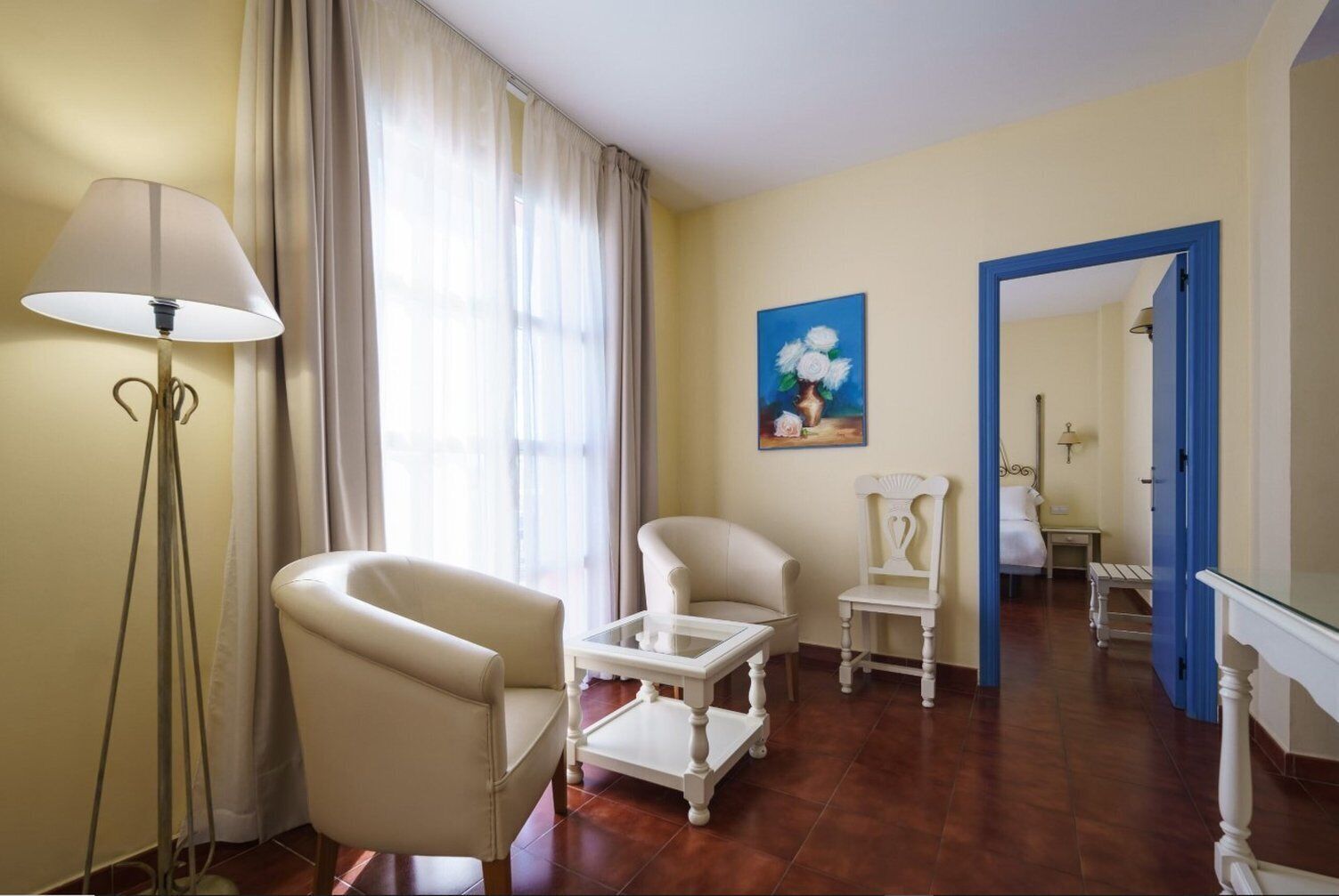 A room with a large window, a floor lamp, a painting, and a chair.