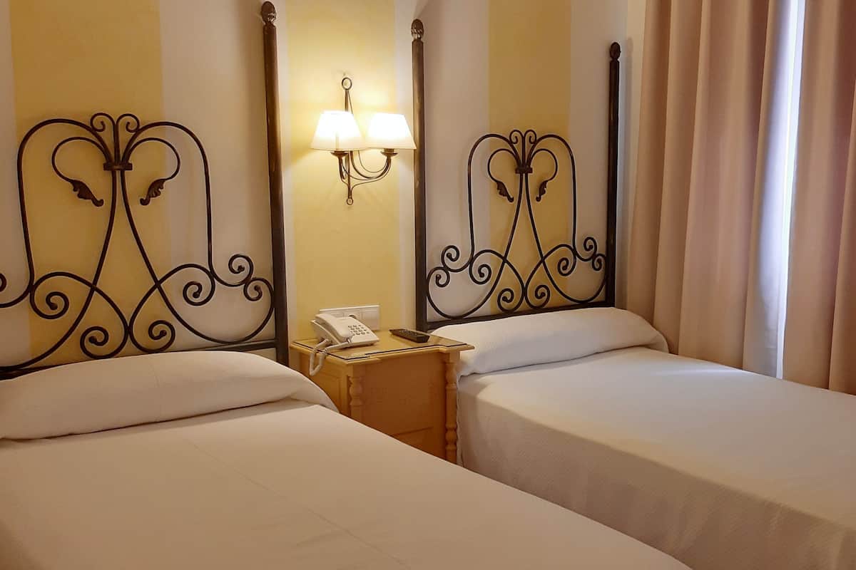A hotel room with two single beds, a bedside table with a phone and a lamp, and a curtain on the window.