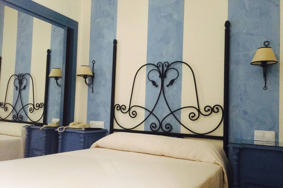 A hotel room with a bed, two bedside tables, a mirror, and wall-mounted lamps.