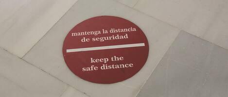 Señal en el suelo con forma circular y texto en español e inglés que indica mantener una distancia segura.