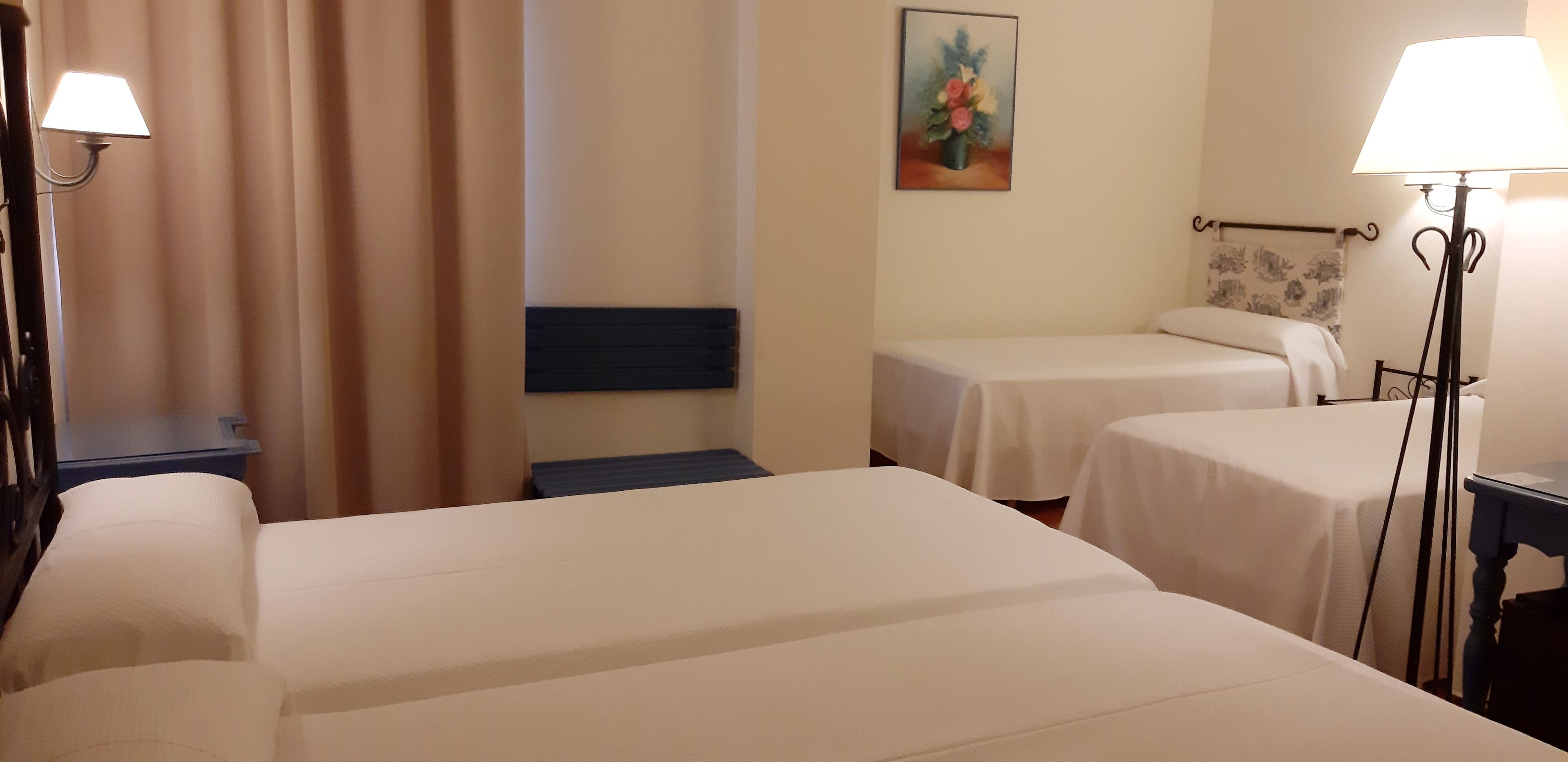 A hotel room with two single beds, a nightstand, a lamp, a painting on the wall, and a curtain.
