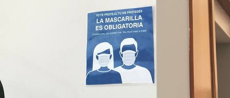 A blue sign on a white wall with text in Spanish and English about mask-wearing.
