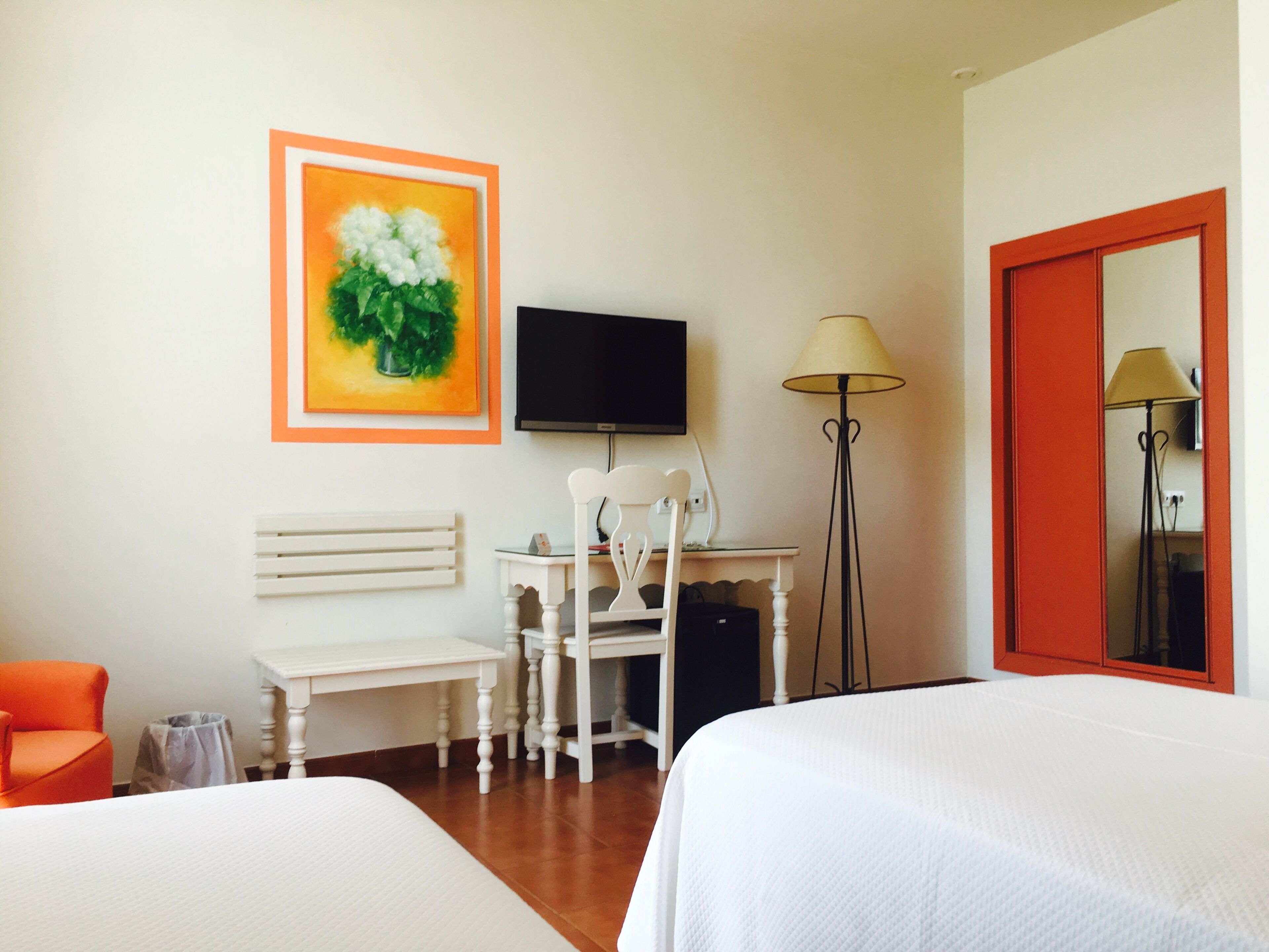 Een hotelkamer met twee bedden, een bureau met stoel, een televisie, een lamp en een schilderij aan de muur.