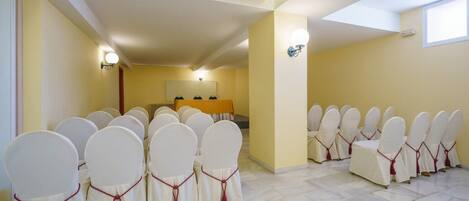 A conference room with rows of chairs and a table, a ceiling with a skylight, and a wall-mounted light fixture.