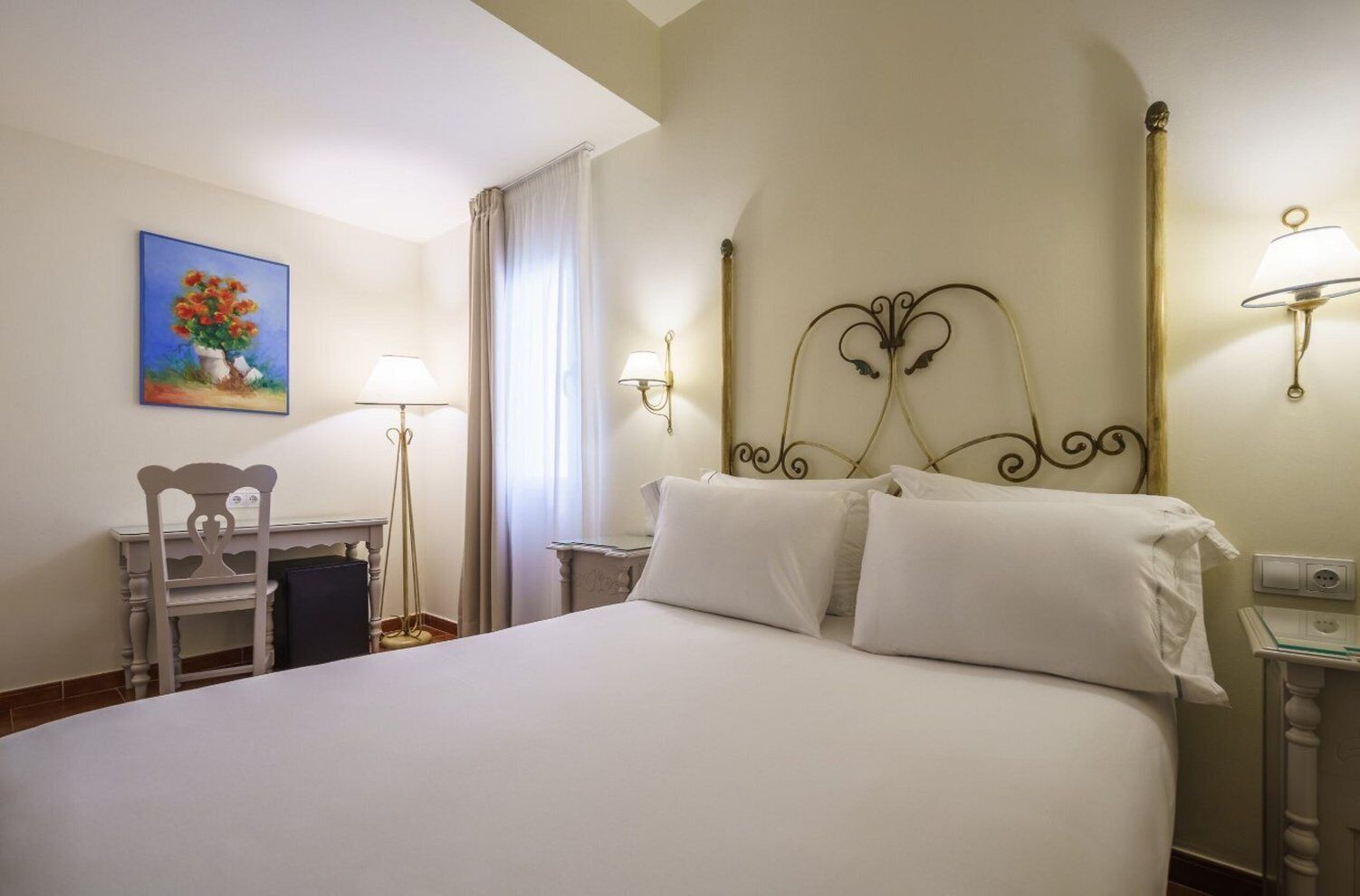Ein Hotelzimmer mit einem großen Bett, einem Schreibtisch mit Stuhl, einem Bild an der Wand und zwei Wandleuchten.