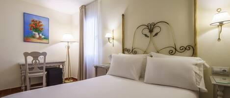 Habitación de hotel con una cama grande, un escritorio con silla, un cuadro en la pared y dos lámparas de pared.